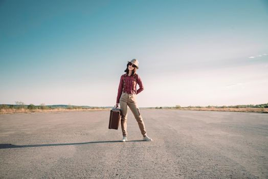 Traveler hipster woman stands on road with vintage suitcase, theme of travel