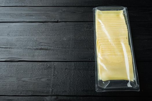 Slices of american cheese plastic pack, on black wooden table with copy space for text