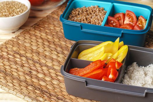 Two lunch boxes with cooked groats and cut vegetables, close up