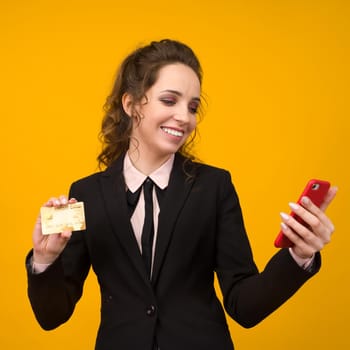 Photo of pleased young woman posing isolated over yellow wall background using mobile phone holding debit card. - image