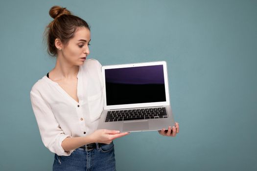 side profile portrait of Beautiful smiling young woman holding netbook computer looking at monitor wearing white shirt isolated on blue background. copy space