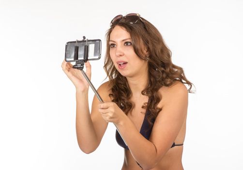 Close up portrait of Tanned adult woman in blue bikini swimsuit taking herself photo with big smatphone on stick