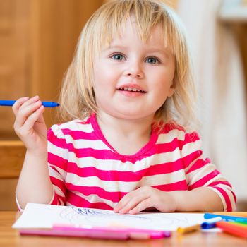 happy three-year-old girl draws felt-tip pens at home