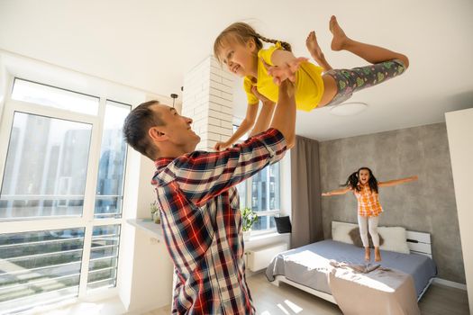 Overjoyed young father holding two little children siblings, having fun together at home, head shot. Excited dad playing with joyful adorable small daughter sisters, enjoying tender weekend moment.