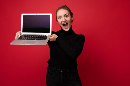 Close-up portrait of Beautiful smiling happy young woman with gathered dark hair holding computer laptop with empty monitor screen with mock up wearing black longsleeve looking at camera.