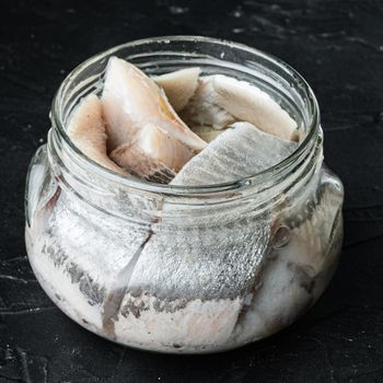 Pickled herring set, in glass jar, on black background, square format