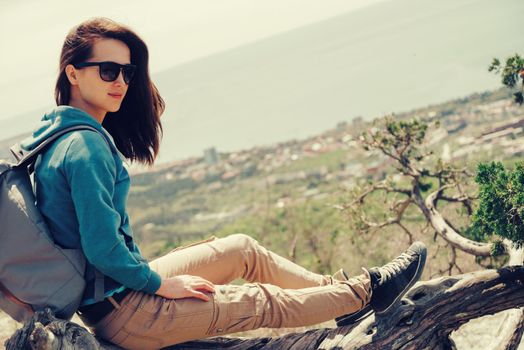 Beautiful traveler young woman resting on tree above the sea in summer. Image with instagram color effect