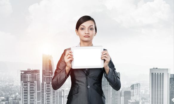 Businesswoman holding tablet computer with blank screen. Beautiful woman in business suit show tablet PC near her face. Corporate businessperson on cityscape background. Digital technology layout.