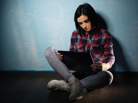 Young sad girl suffering from dependence on social networks sitting on the floor with a notebook
