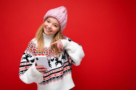 Photo shot of attractive smiling positive good looking young woman wearing casual stylish outfit poising isolated on background with empty space holding in hand and using mobile phone messaging sms looking at camera.