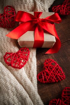 Gift box with red ribbon and hearts. Gift for Valentine's Day in a box with a red ribbon on the background of hearts and a cozy knitted pullover, vertical photo