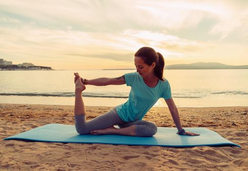 Young woman doing yoga exercise on summer sand beach at sunset, workout