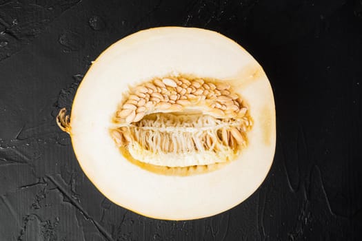 Sugar melon cut in half set, on black dark stone table background, top view flat lay