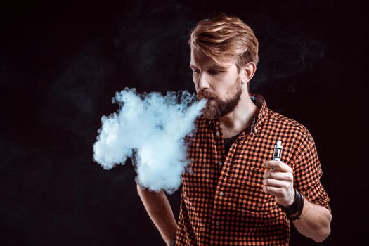 young man wearing a plaid shirt smokes an electronic cigarette on a black background