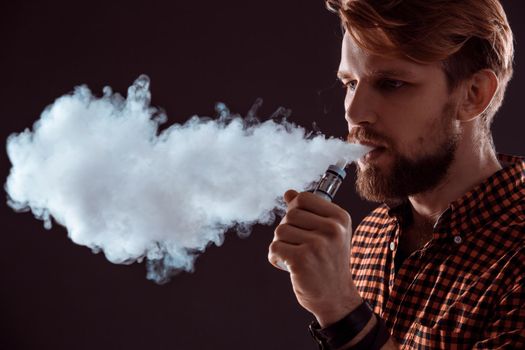 young man wearing a plaid shirt smokes an electronic cigarette on a black background