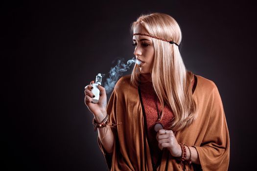 Young woman in the Boho style blowing smoke. The blonde on a dark background