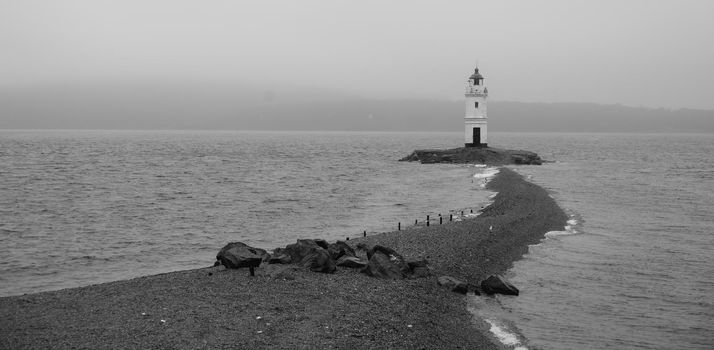 Lighthouse on foreland in the sea, black and white image