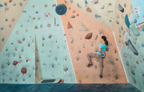 Free climber young woman exercises to climbing artificial boulder indoor, bouldering. Climber putting her hand in the bag of powder magnesia