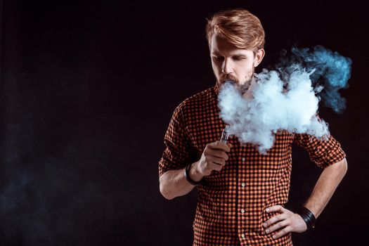 young man wearing a plaid shirt smokes an electronic cigarette on a black background