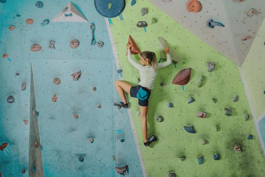 Climber little girl exercises on artificial boulders wall in gym