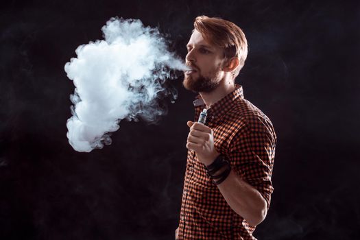 young man wearing a plaid shirt smokes an electronic cigarette on a black background