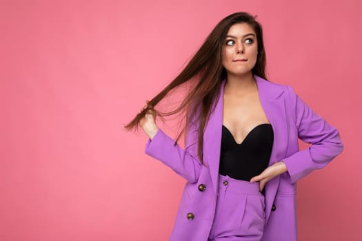 Portrait of thoughtful beautiful fashionable brunette woman in casual trendy violet jacket isolated on pink background with free space.