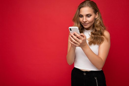 Beautiful young woman wearing casual clothes standing isolated over background surfing on the internet via phone looking at mobile screen.