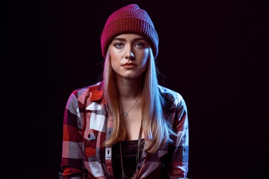 Charming casual girl, wearing in red and black plaid shirt and hat on a black background. Young woman looking into the camera