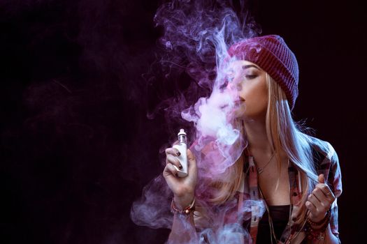 young woman smoking electronic cigarette on black background. Copy space