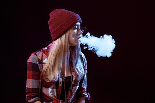 young woman smoking electronic cigarette on black background. Copy space