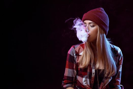 young woman smoking electronic cigarette on black background. Copy space