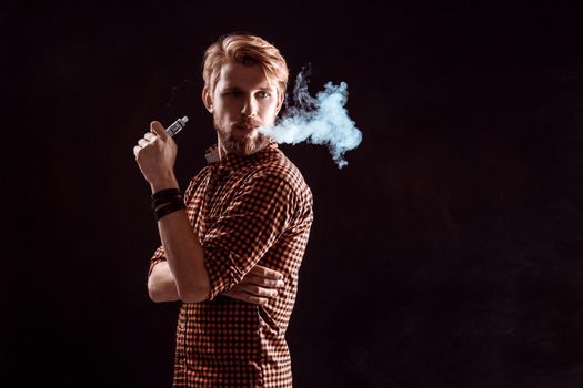 young man wearing a plaid shirt smokes an electronic cigarette on a black background