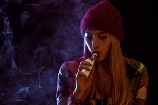 young woman smoking electronic cigarette on black background