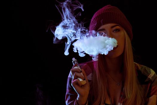 young woman smoking electronic cigarette on black background. woman looking at the camera