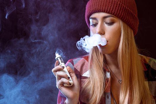 young woman smoking electronic cigarette on black background. Copy space