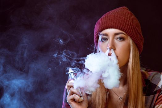 young woman smoking electronic cigarette on black background. Copy space. woman looking at the camera