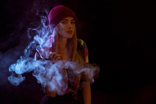 young woman smoking electronic cigarette on black background. woman looking at the camera