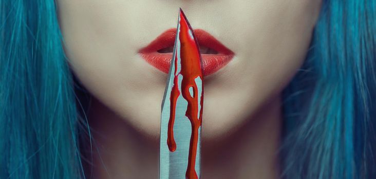 Young woman kissing a knife in blood. Halloween or horror theme. Close-up image of red lips