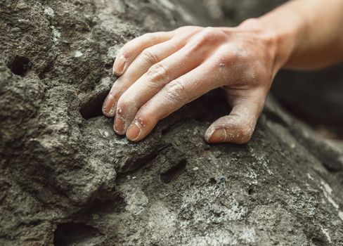 Woman climbing on rock outdoor, close-up image of climber hand in magnesium powder