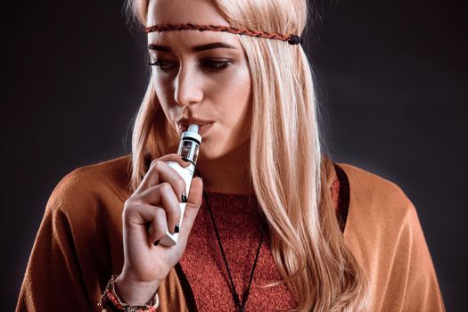 Young woman in the Boho style blowing smoke. The blonde on a dark background. Close-up