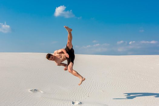 Portrait of young parkour man doing flip or somersault on the sand. Freezed moment of beginning doing bounce.