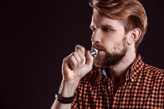 young man wearing a plaid shirt smokes an electronic cigarette on a black background