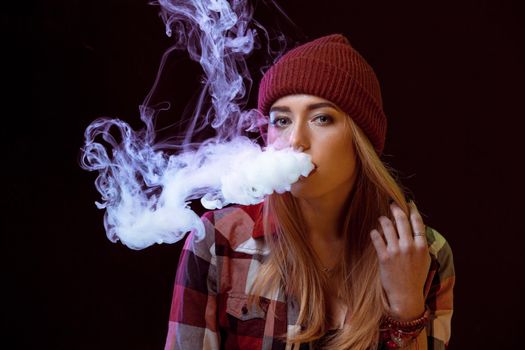 young woman smoking electronic cigarette on black background. woman looking at the camera