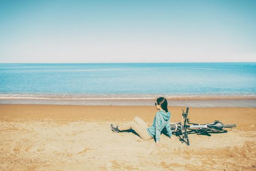 Beautiful young woman resting near a bicycle on beach in summer. Image with instagram color effect