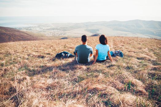 Loving couple sitting on mountain meadow and enjoying view of nature. Image with color effect