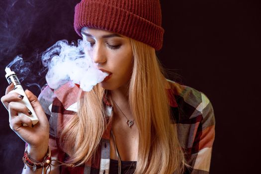 young woman smoking electronic cigarette on black background