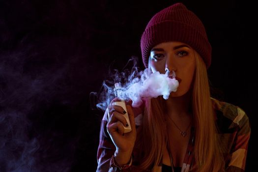 young woman smoking electronic cigarette on black background. woman looking at the camera