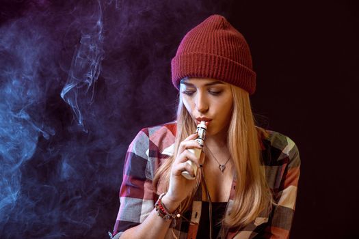 young woman smoking electronic cigarette on black background