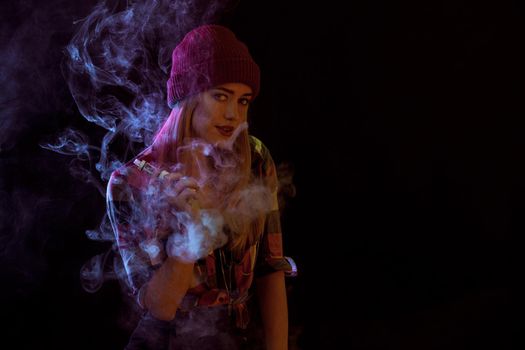 young woman smoking electronic cigarette on black background. woman looking at the camera