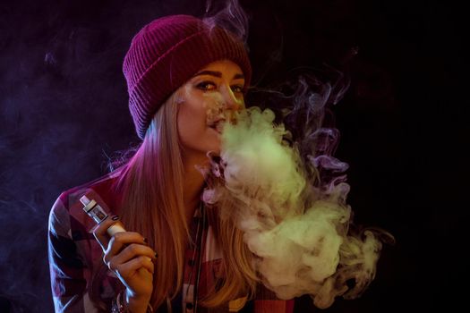 young woman smoking electronic cigarette on black background. woman looking at the camera